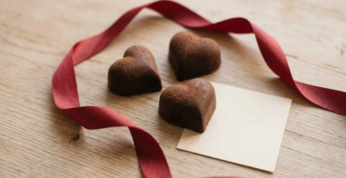 Chocolats artisanaux en forme de cœur disposés avec un ruban rouge sur une surface claire, évoquant un cadeau romantique.